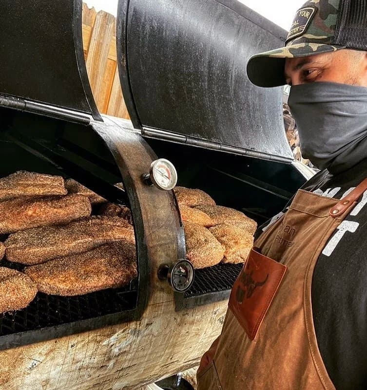 Pitmaster Ryan with BBQ smoked meats at the wood-fired smoker